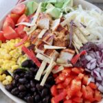 salad in bowl topped with black beans, corn and diced grilled chicken