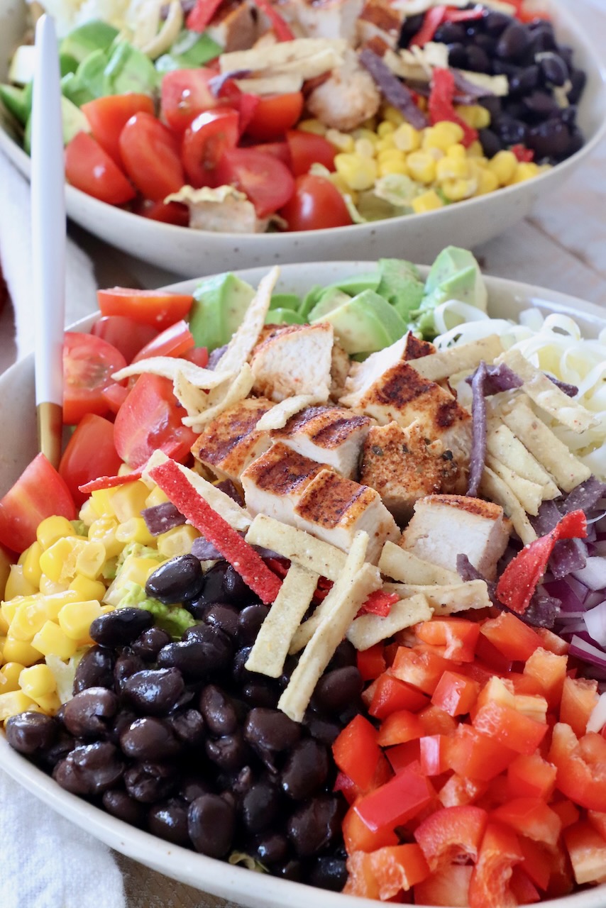 salad in bowl topped with black beans, corn and grilled chicken