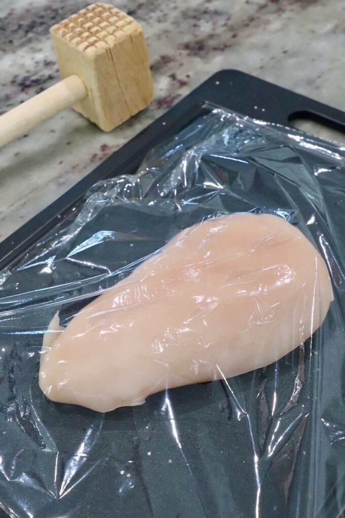 chicken breast on cutting board covered with plastic wrap