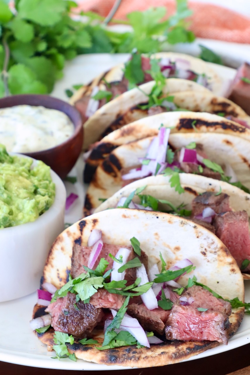 steak tacos on plate with a small bowl of guacamole on the side