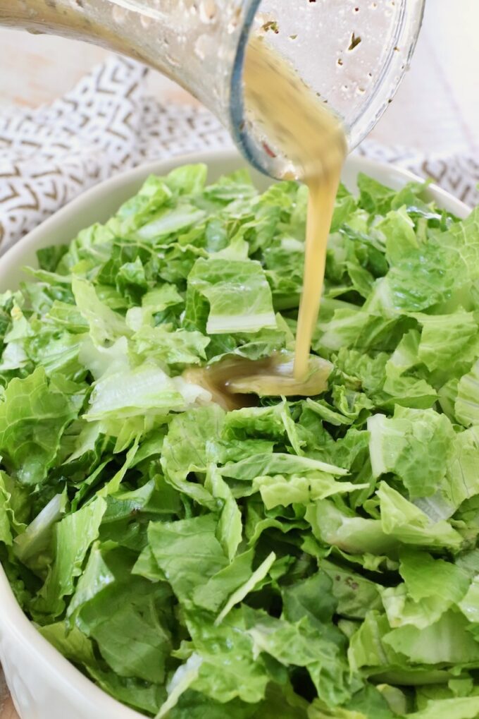 salad dressing poured onto a bowl of chopped greens