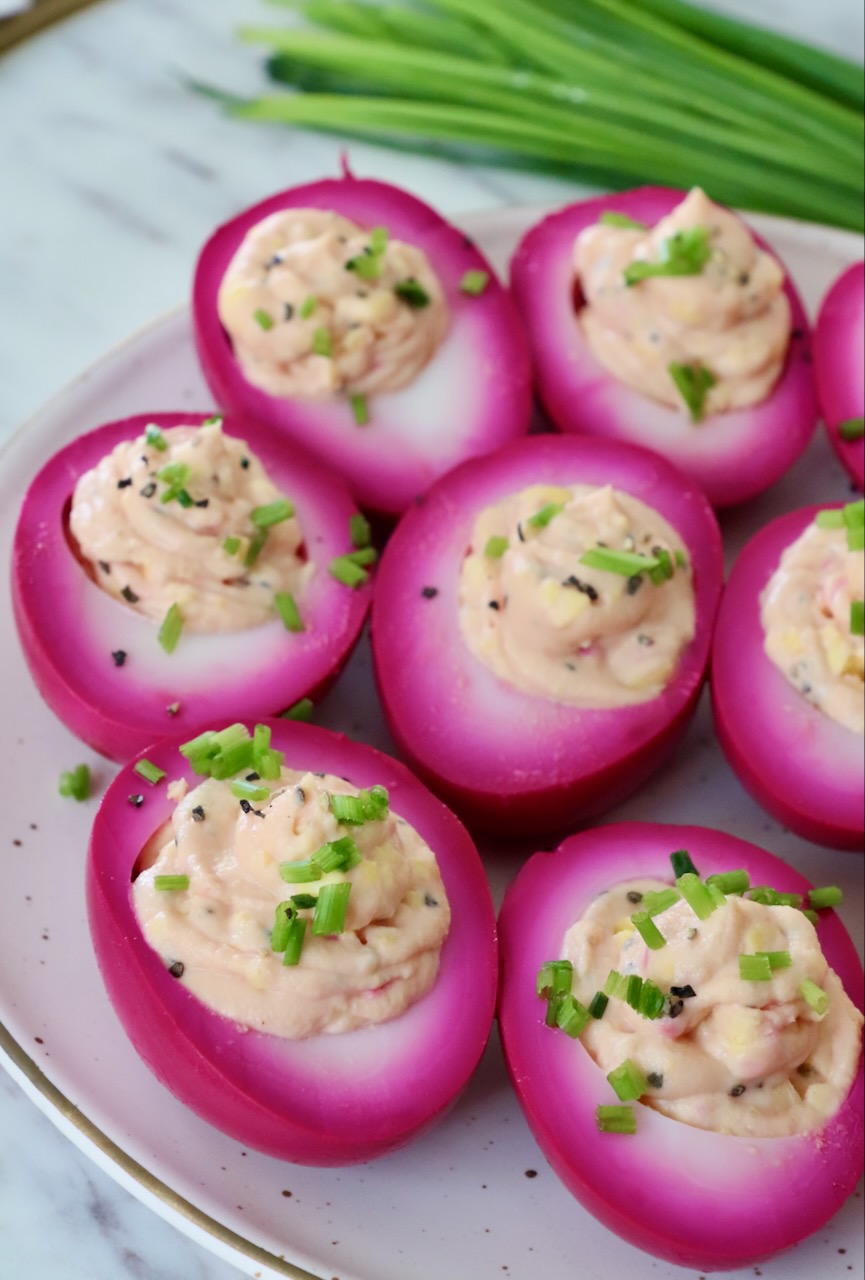 beet pickled deviled eggs on plate topped with fresh chives