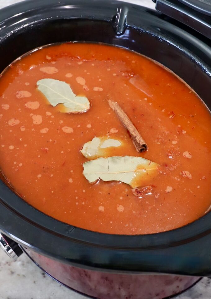 chili tomato sauce in slow cooker topped with bay leaves and cinnamon stick