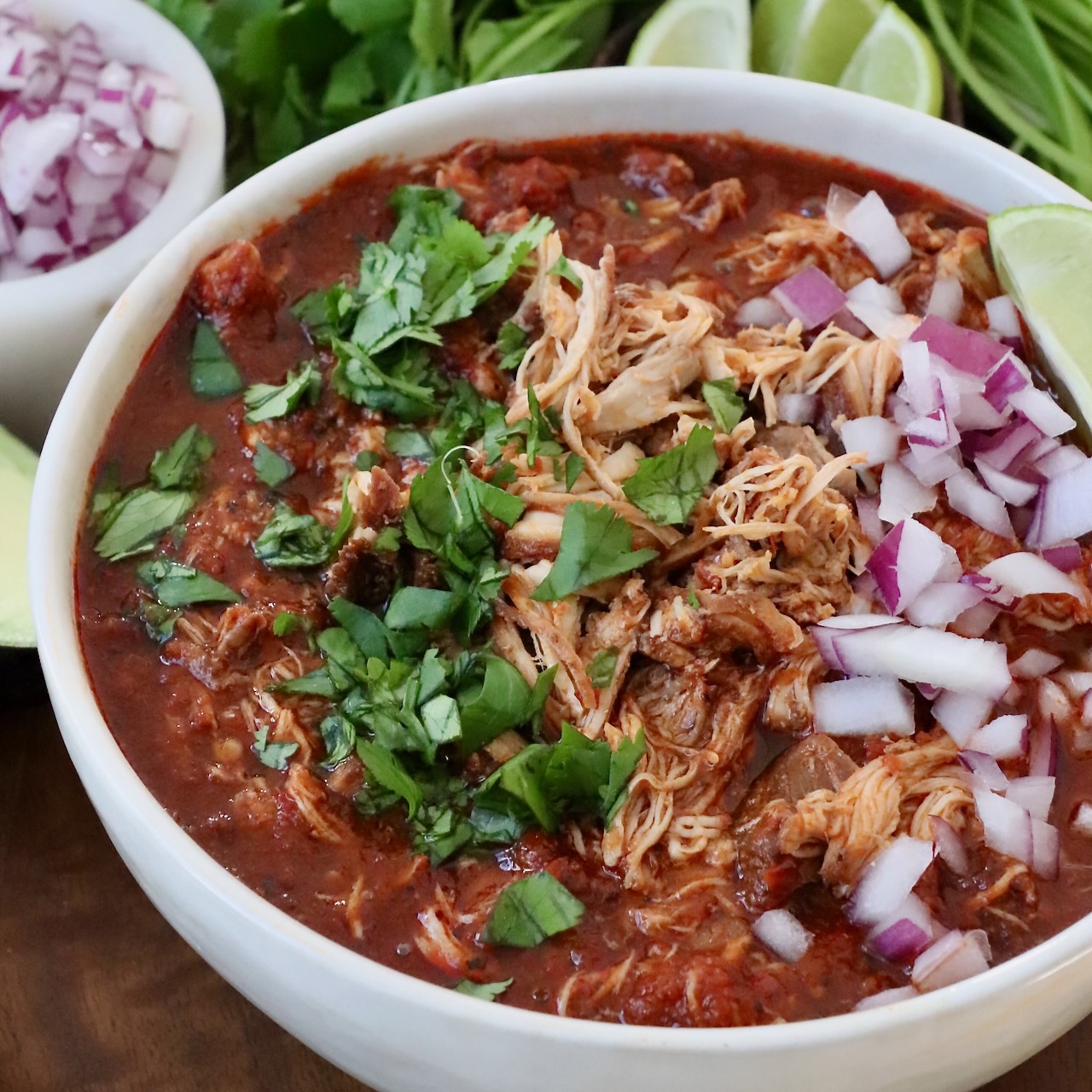 shredded chicken with birria broth in bowl topped with diced onions and cilantro