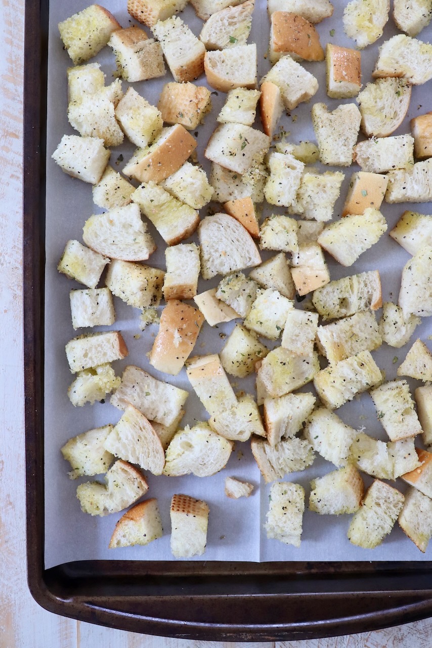 seasoned cubes of bread on parchment lined baking sheet