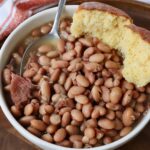 cooked pinto beans in bowl with spoon and cornbread