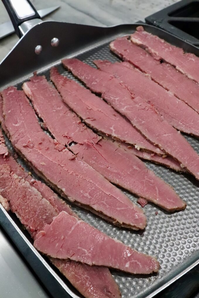 slices of corned beef on griddle pan on stove