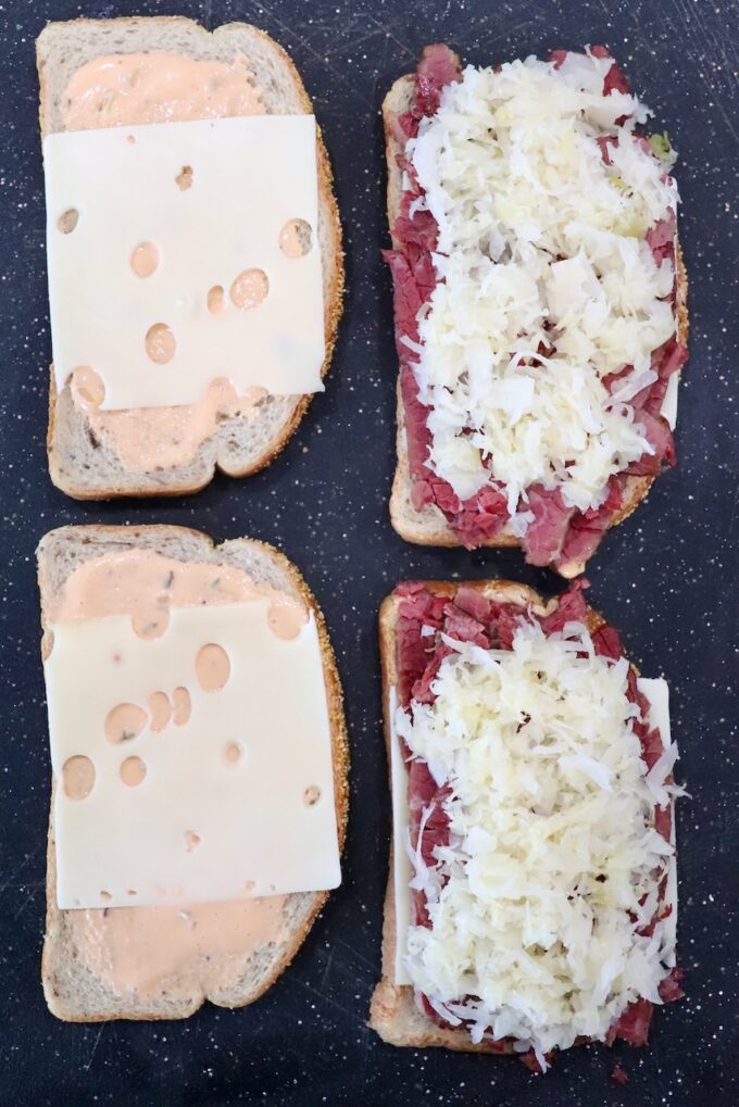 slices of bread, topped with swiss cheese and corned beef on cutting board 
