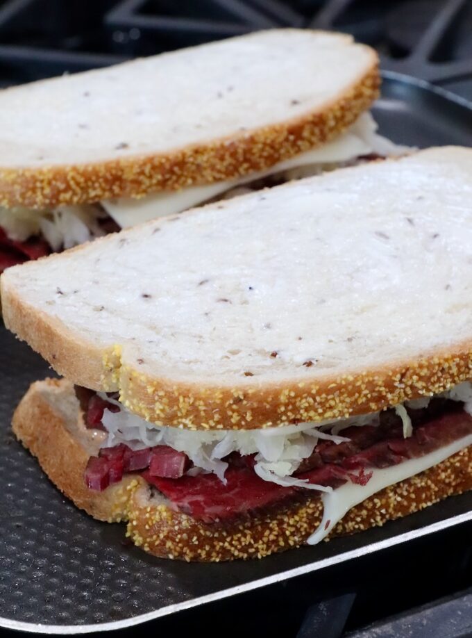 uncooked reuben sandwiches on griddle pan on stove