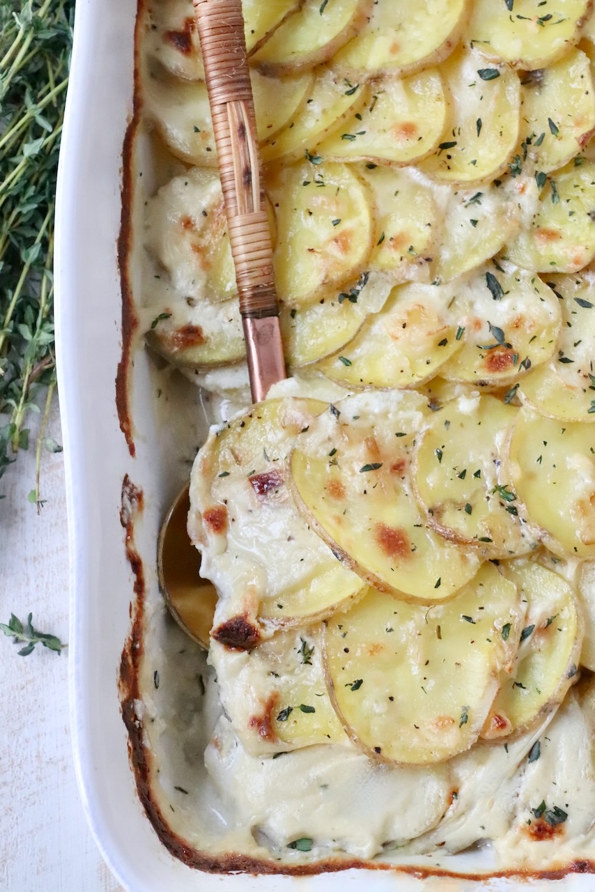 cooked scalloped potatoes in baking dish with serving spoon