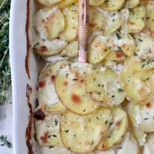 cooked scalloped potatoes in casserole dish with serving spoon