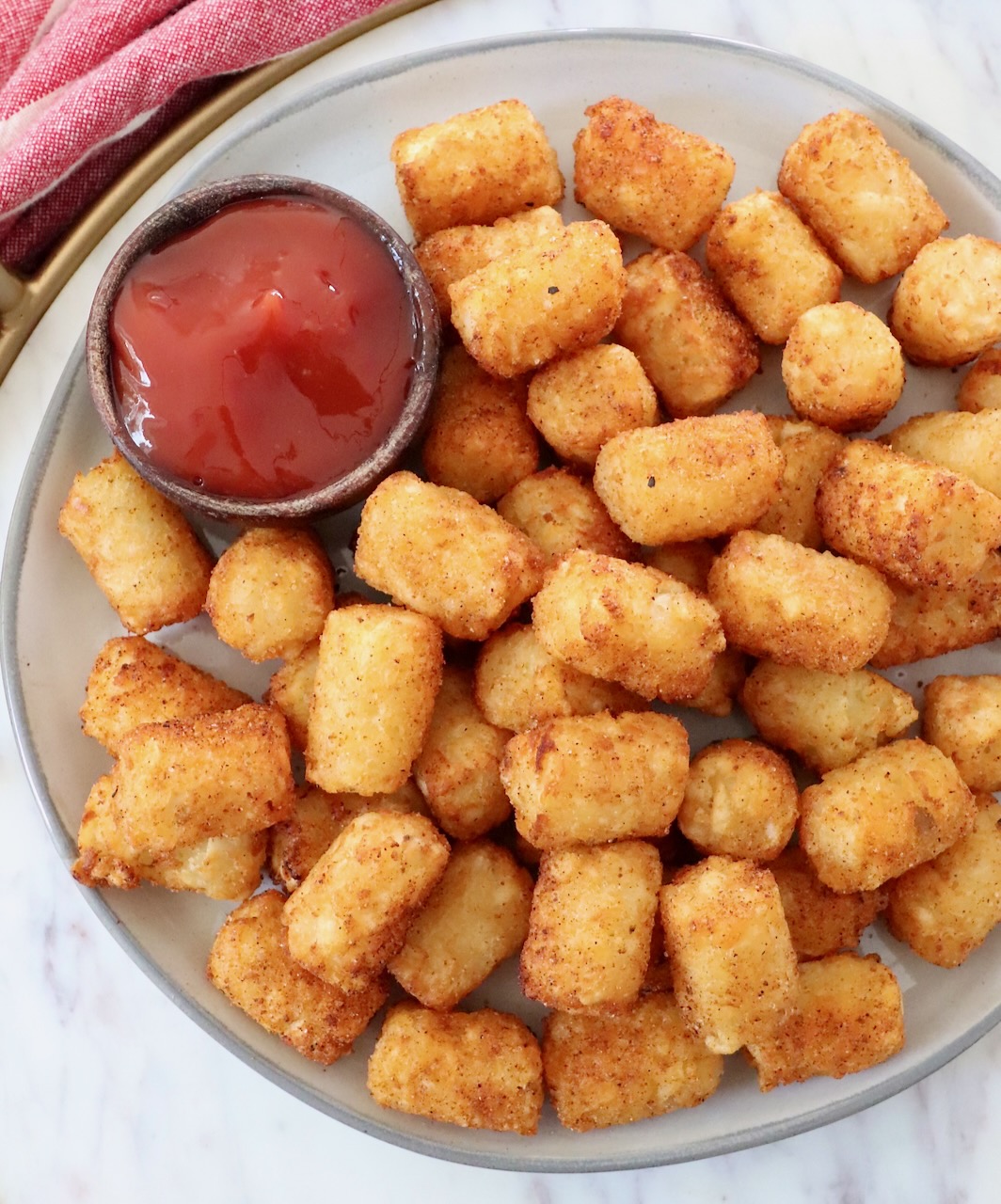cooked seasoned tater tots on plate with small bowl of ketchup