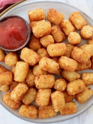cooked tater tots on plate with small bowl of ketchup