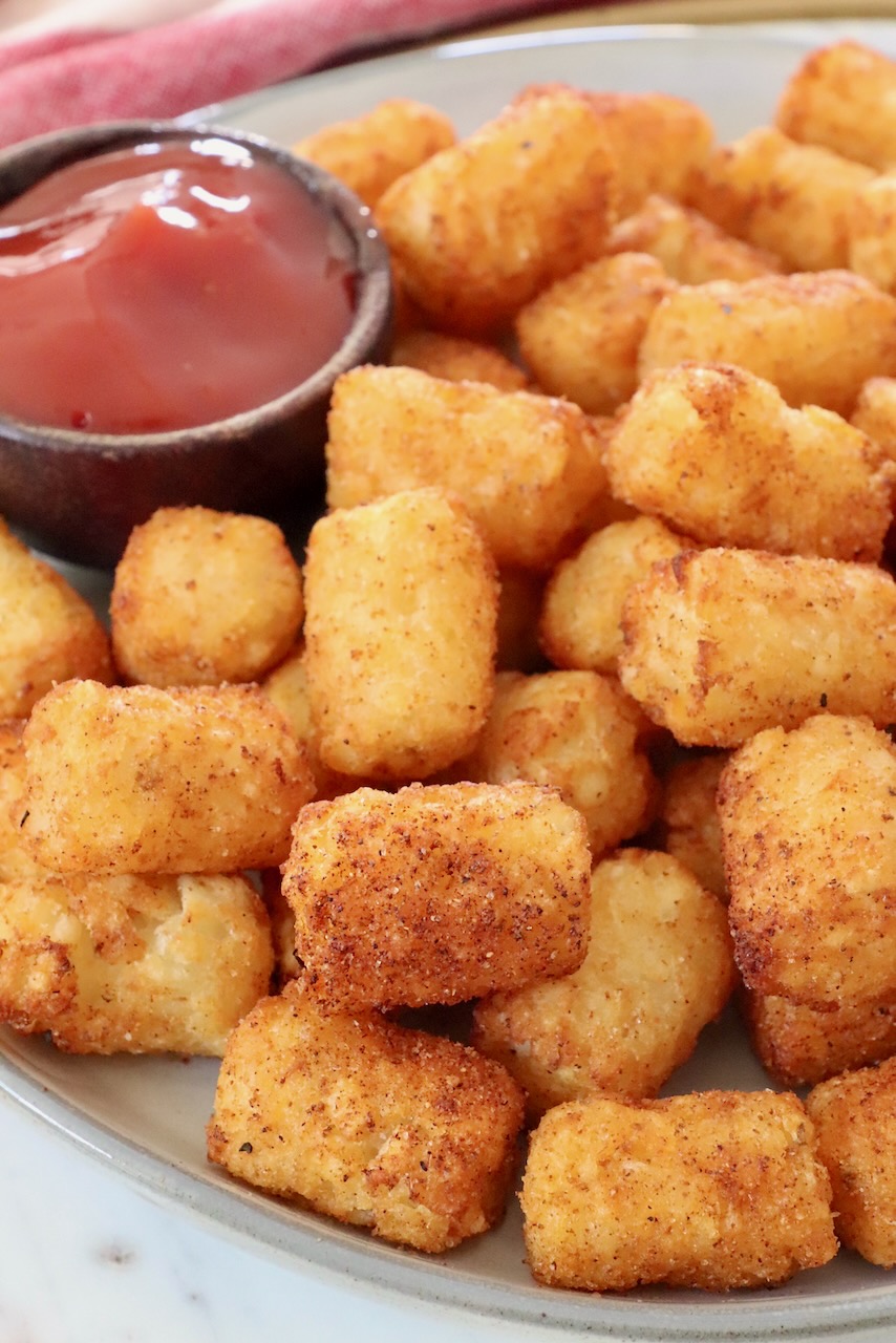 cooked tater tots on plate with small side dish of ketchup