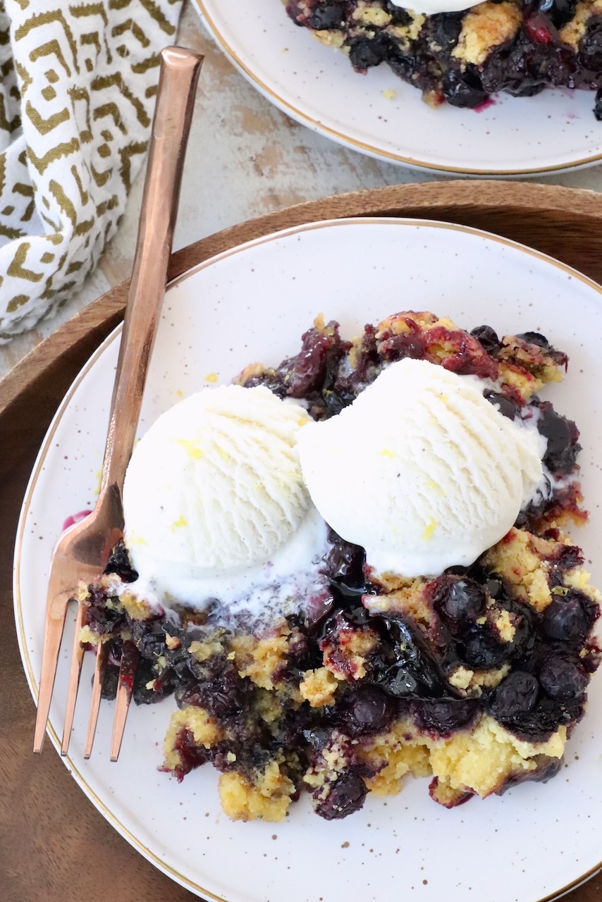 blueberry dump cake on plate with fork, topped with scoops of vanilla ice cream