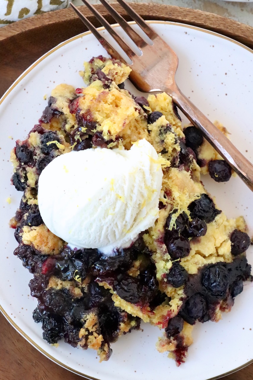 blueberry dump cake on plate with fork and a scoop of vanilla ice cream