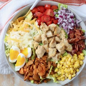 salad in bowl topped with crispy chicken, corn, cheese, bacon and veggies