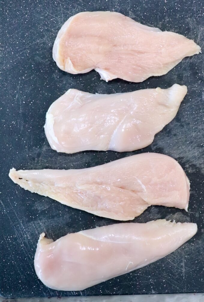 four halves of chicken breasts on cutting board