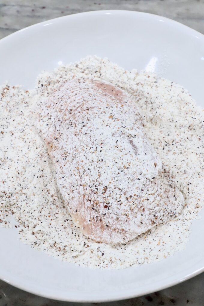 chicken breast in bowl of seasoned flour