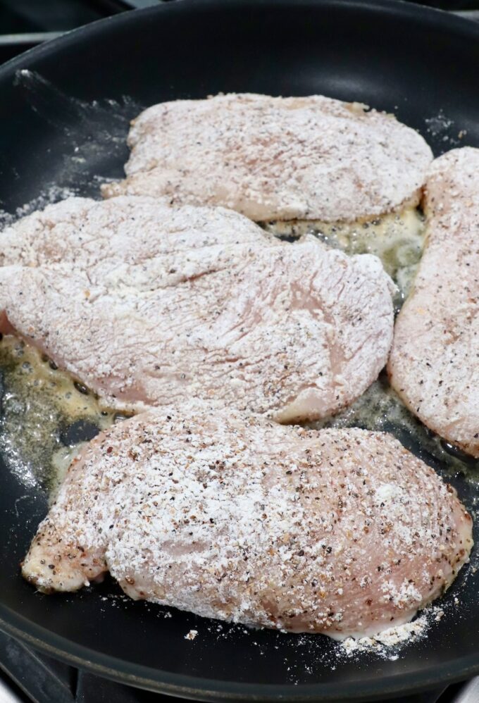 seasoned chicken breasts cooking in butter in skillet