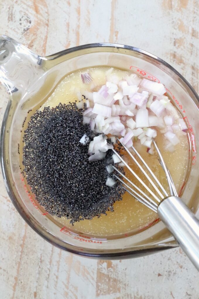 poppyseeds and minced shallots in glass bowl of salad dressing with whisk
