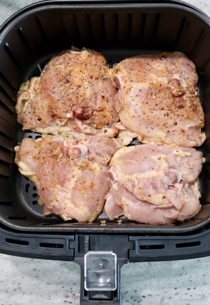 seasoned raw bone-in chicken thighs in air fryer basket