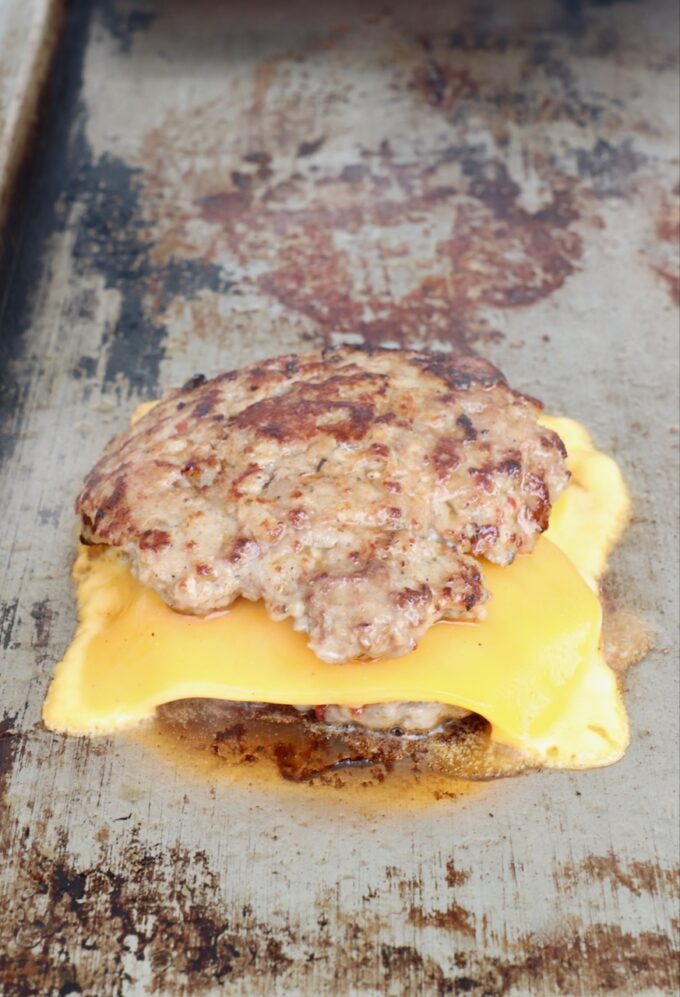 two burger patties on top of each other with a slice of cheese in the middle on a flat top
