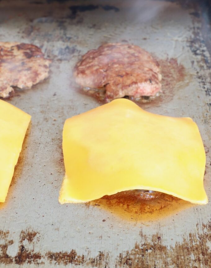 sliced of cheese on top of cooked burger patties on flat top
