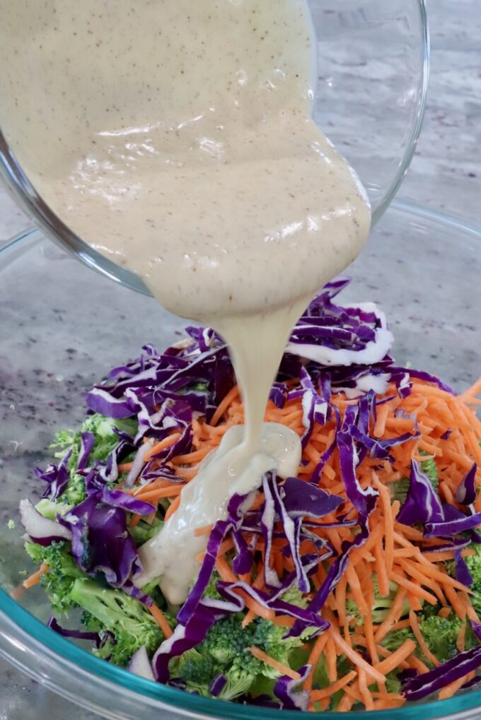 broccoli slaw in bowl with dressing poured over the slaw