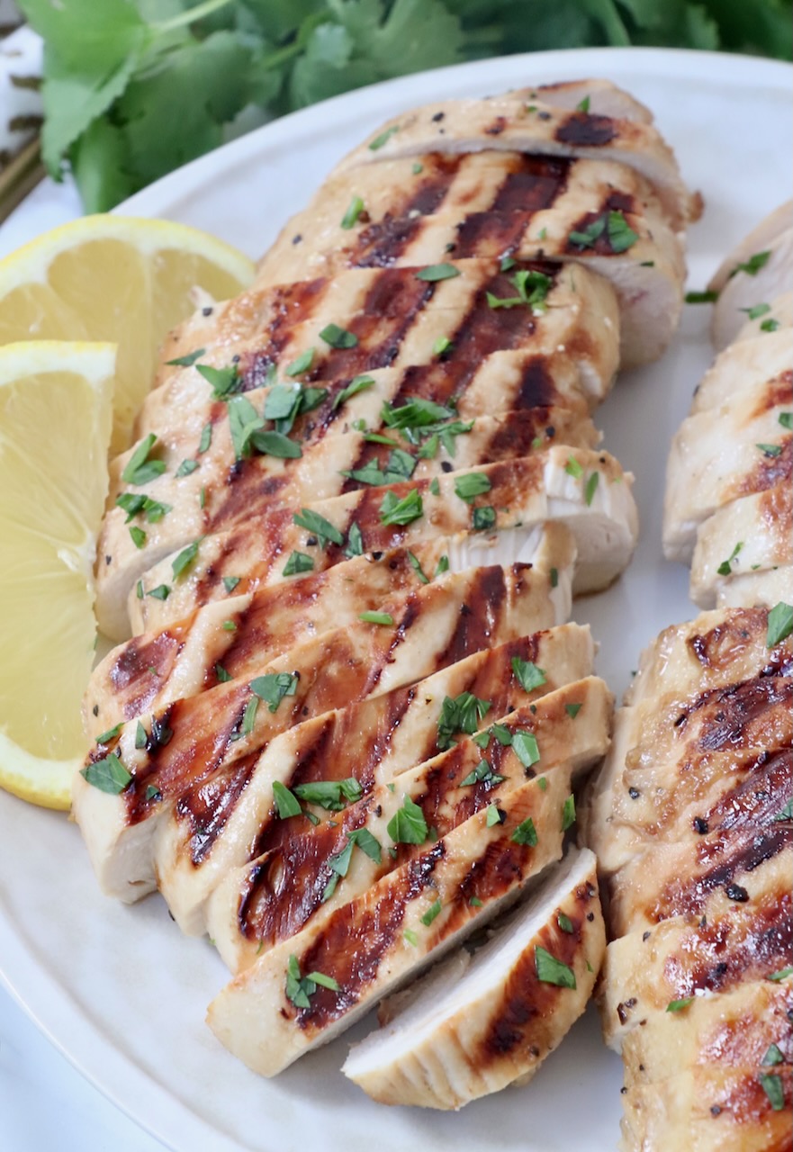 sliced grilled chicken on plate with lemon wedges