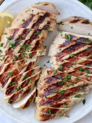 sliced grilled chicken on plate with lemon wedges