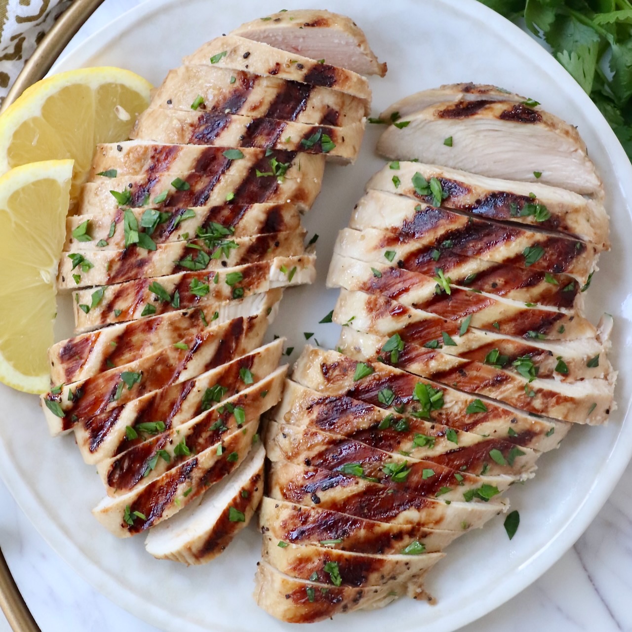 sliced grilled chicken on plate with lemon wedges