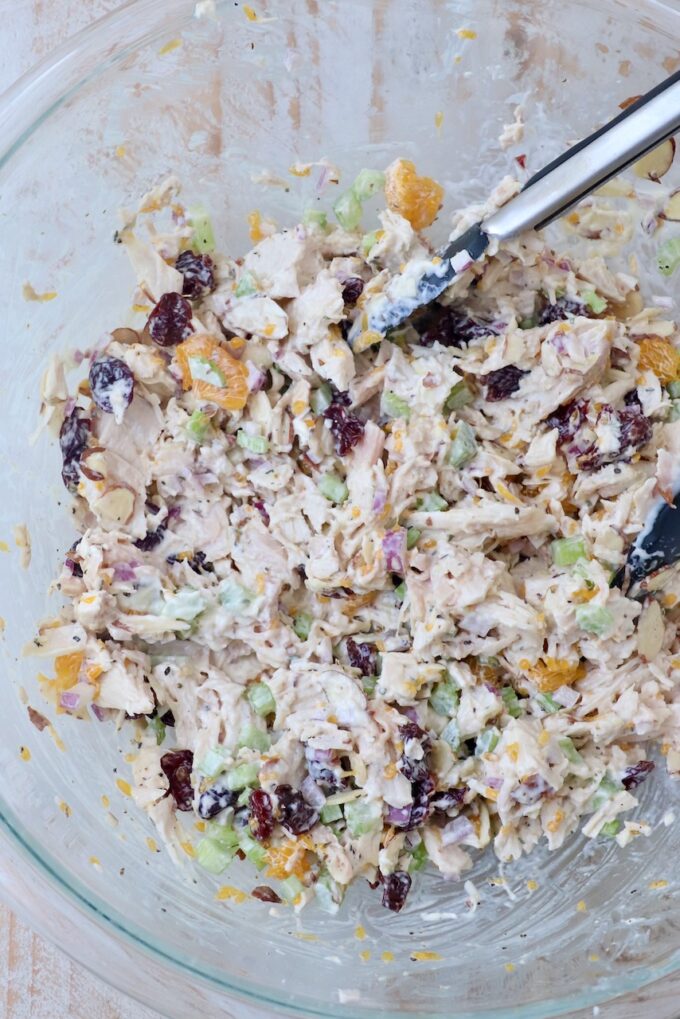 chicken salad prepared in a large glass bowl with kitchen tongs
