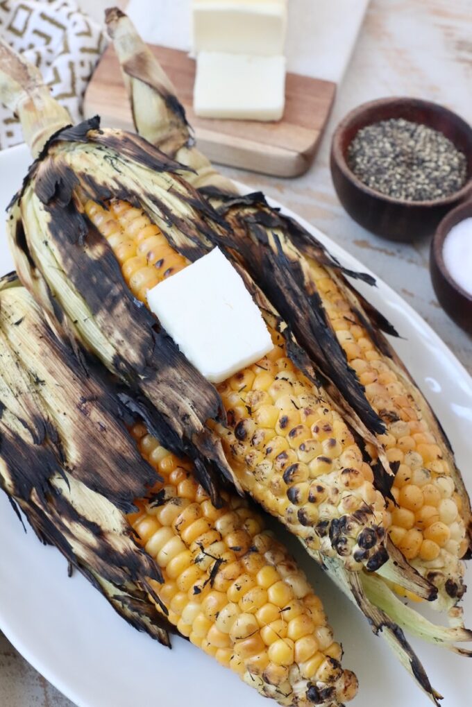 grilled corn with husks on plate with butter on top