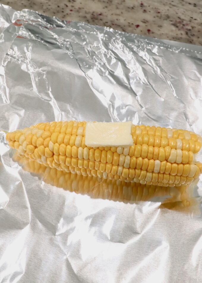 corn on the cob with the husks removed on piece of foil with slice of butter on top