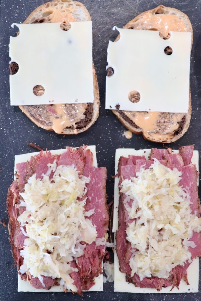 swiss cheese, sliced pastrami and sauerkraut on slices of rye bread on cutting board