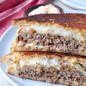 cooked patty melt sandwich cut in half on plate
