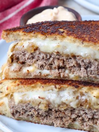 cooked patty melt sandwich cut in half on plate