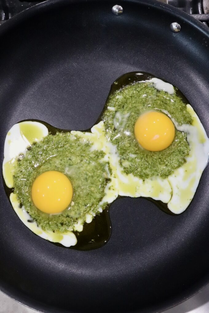 eggs cracked on top of pesto in skillet
