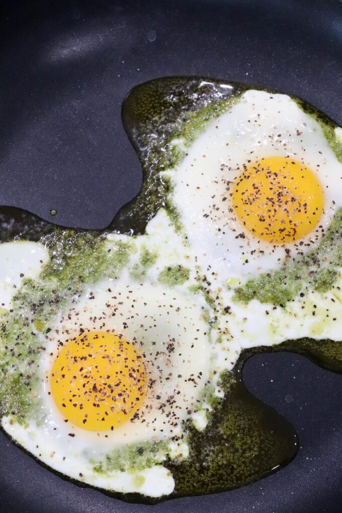 cooked eggs on top of pesto in skillet, seasoned with salt and pepper