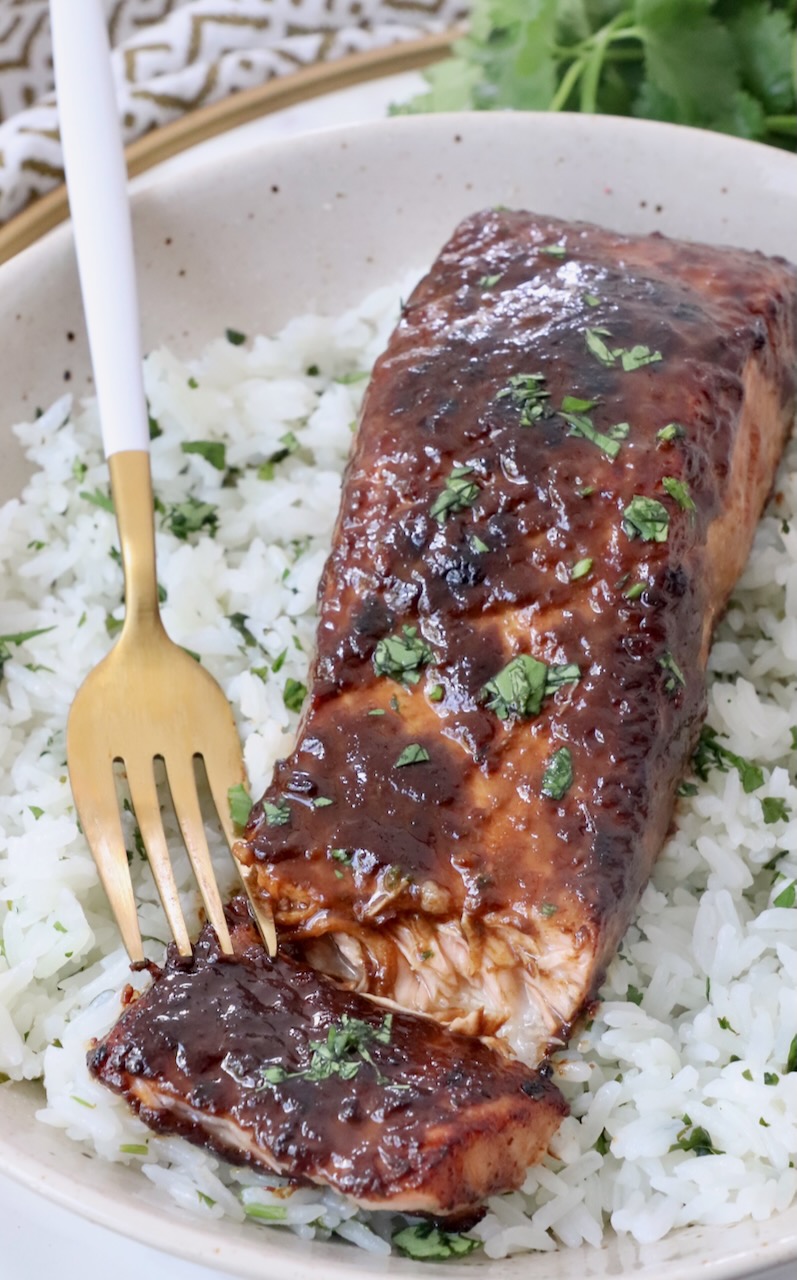 cooked glazed piece of salmon on top of rice in bowl with fork