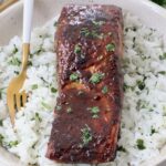 cooked glazed salmon on top of white rice in bowl with fork