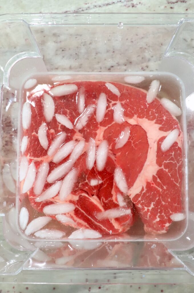 chuck roast in brine with ice cubes in plastic tub