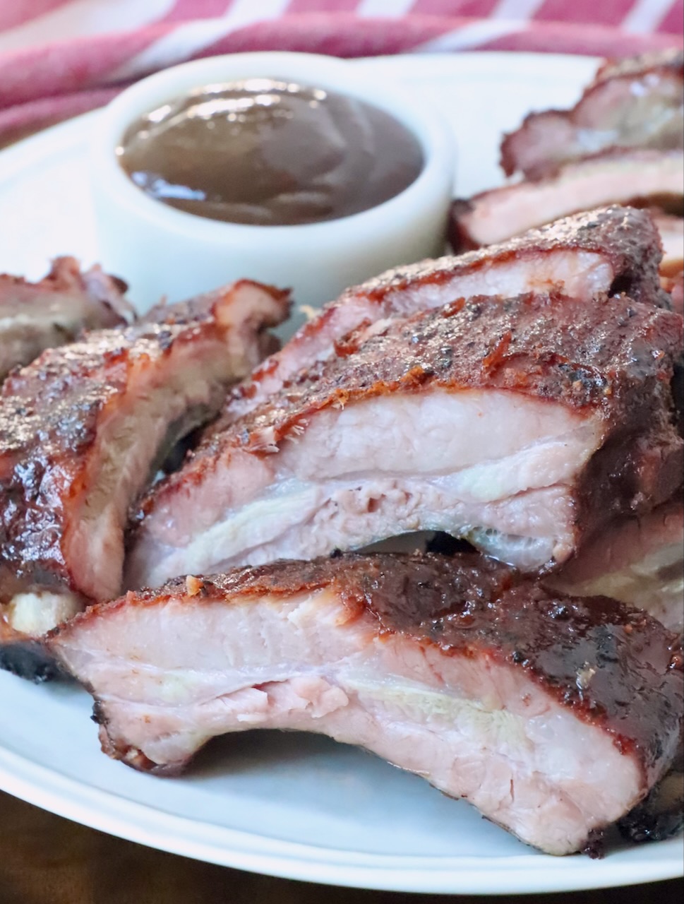 sliced smoked baby back ribs on a plate with a small bowl of bbq sauce