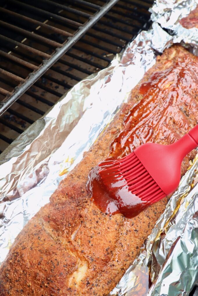 bbq sauce brushed on rack of ribs with a kitchen brush, on top of a piece of foil