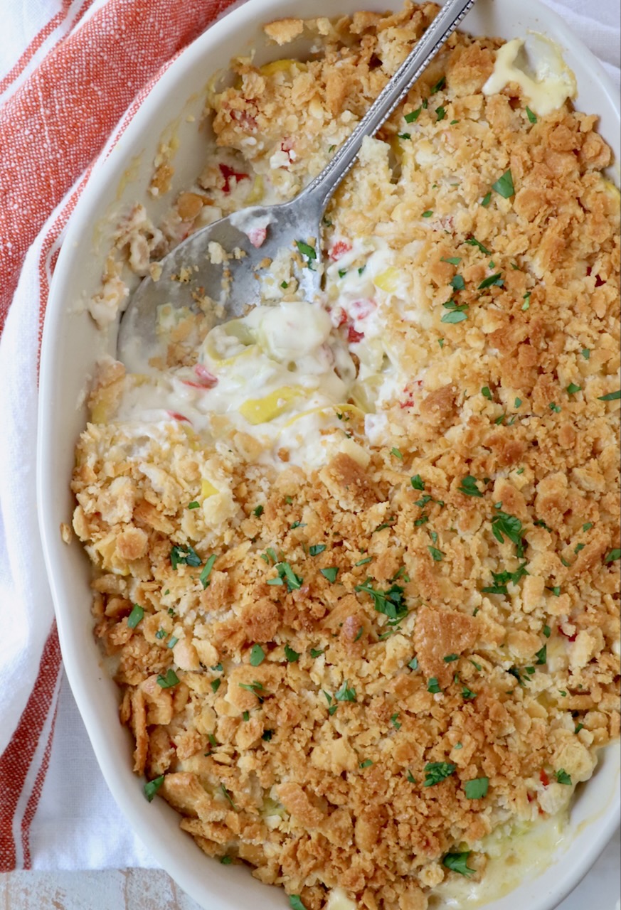 squash casserole topped with ritz cracker topping in baking dish with serving spoon