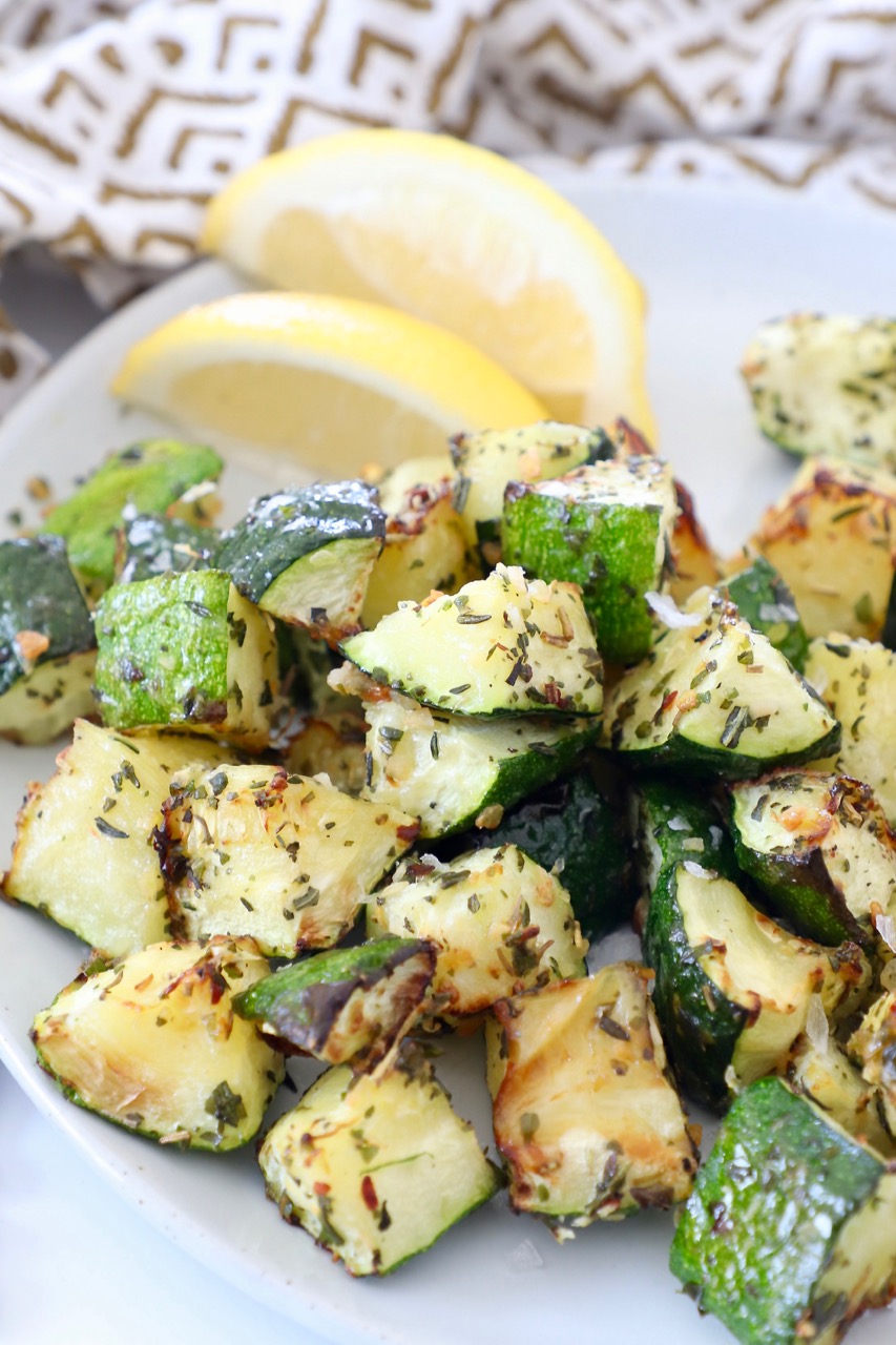 seasoned cooked diced zucchini on plate with lemon wedges