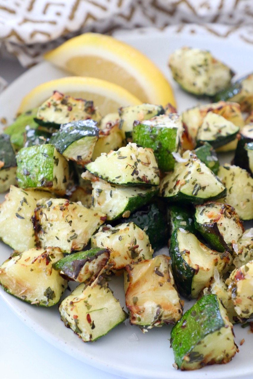 diced cooked zucchini on plate with lemon wedges