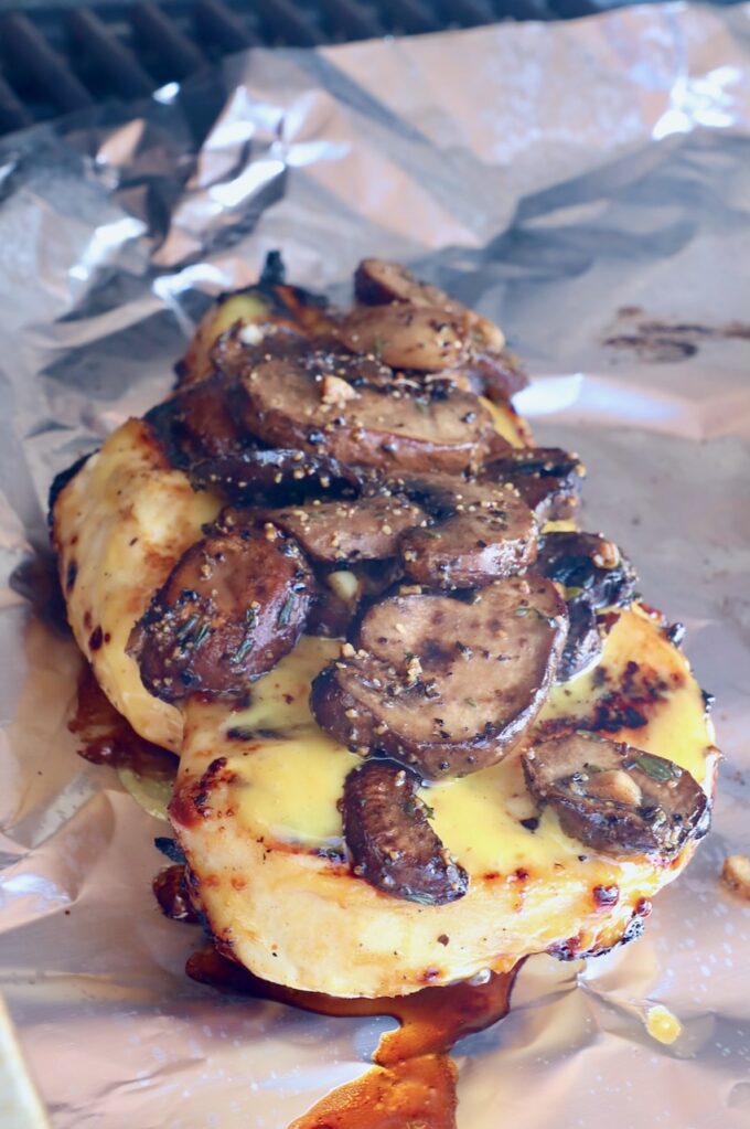 grilled chicken topped with mushrooms on a piece of foil in a grill