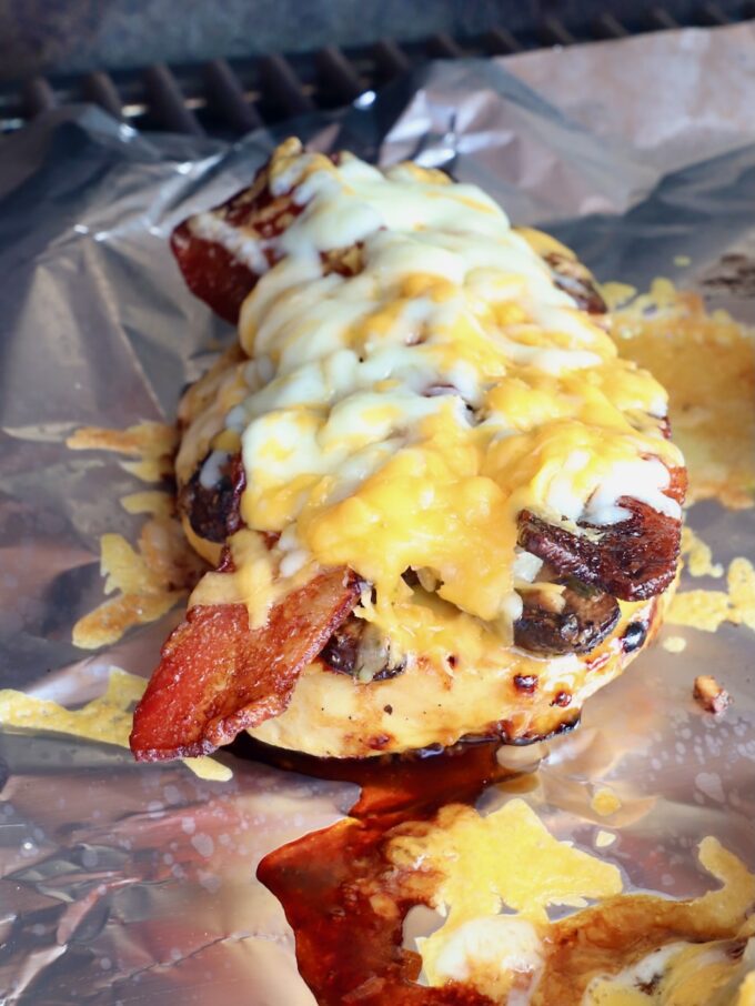 grilled chicken topped with slices of bacon and melted cheese on a piece of foil in a grill